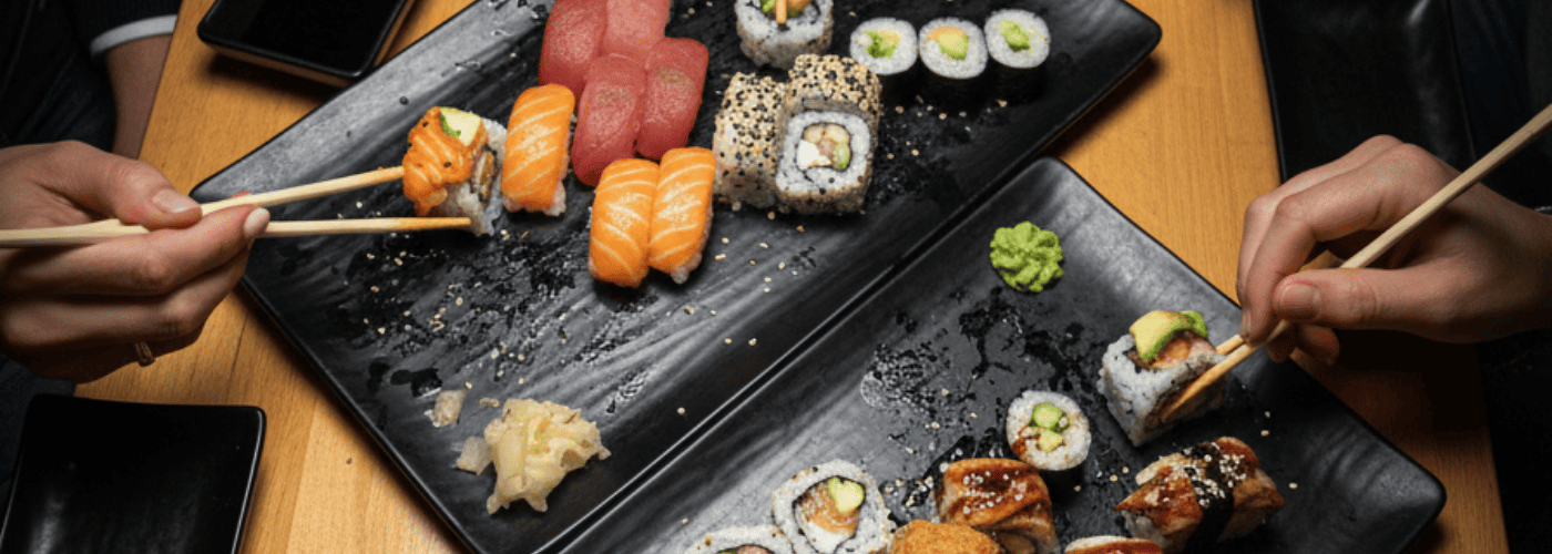 Imagen de varias personas compartiendo sushi con palillos en una mesa, con bandejas de nigiris, makis y piezas variadas. Acompaña la sección del blog sobre sushi en grupo y refuerza la importancia de pedir con orden, escuchar a la mesa y disfrutar el Menú
